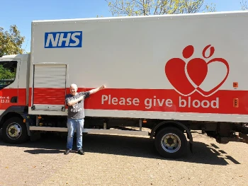 David Harriman stood next to an NHS blood donor van. There is text on the van that reads "Please give blood"