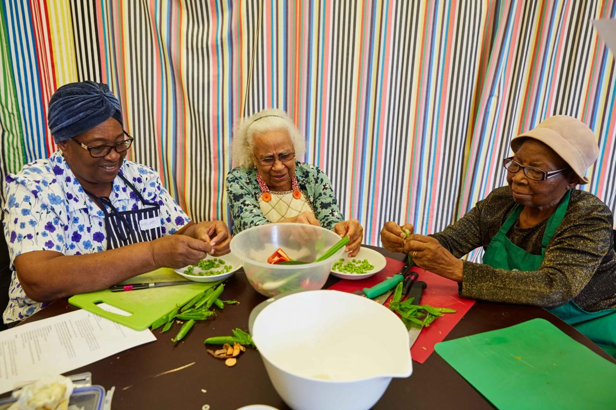 three women sat at a table cutting vegetables