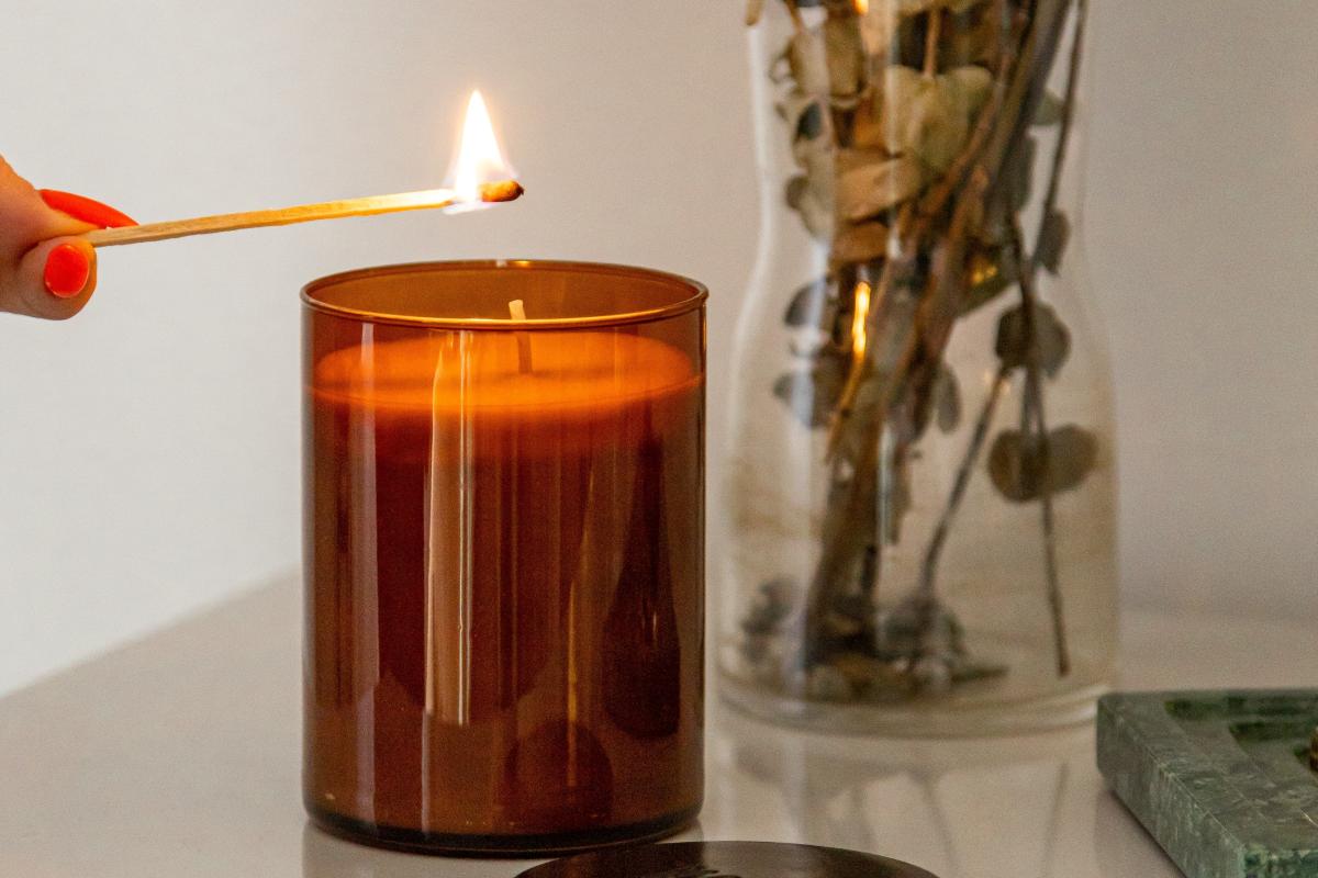 Hand lighting a candle in a brown glass jar on a white table