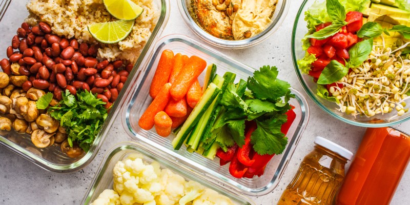 Healthy vegan food in glass containers, top view. Rice, beans, vegetables, hummus and juice. 