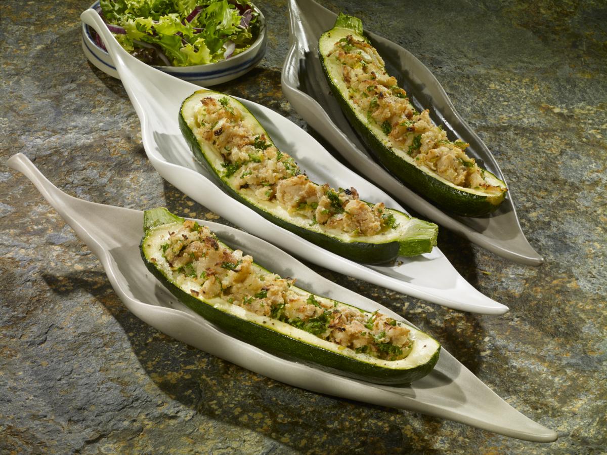 Three leaf shaped shallow bowls filled with half courgettes that are stuffed with almonds